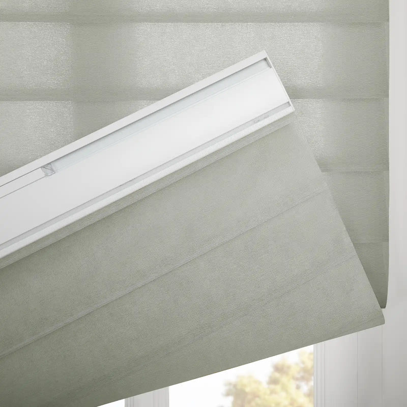 A light green pleated fabric window Blind partially lowered, showcasing its woven texture, white headrail, and a blurred view of outdoor greenery