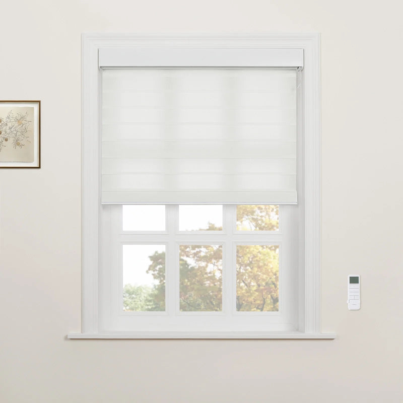 A white layered Roman Blind partially lowered over a white multi-paned window with a wall-mounted remote control on the wall