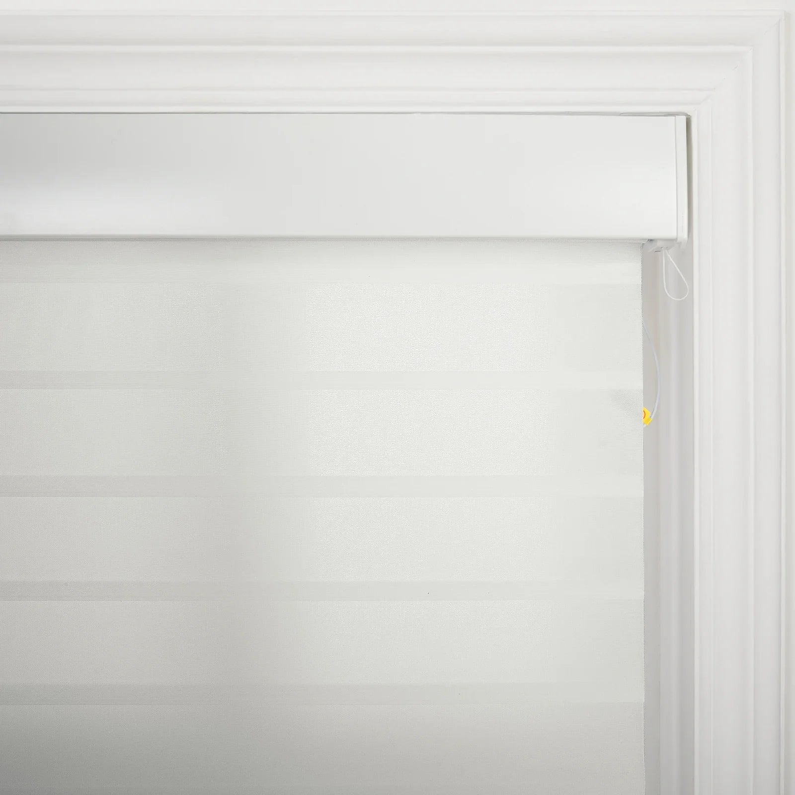 A white roller window Blind featuring alternating sheer and opaque horizontal stripes within a decorative white window frame, accented by a white pull cord with a small yellow bead