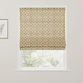 A Roman blind at a window featuring a beige background with a repeating pattern of terracotta red ovals and green leaf motifs, with a framed botanical print on the adjacent wall