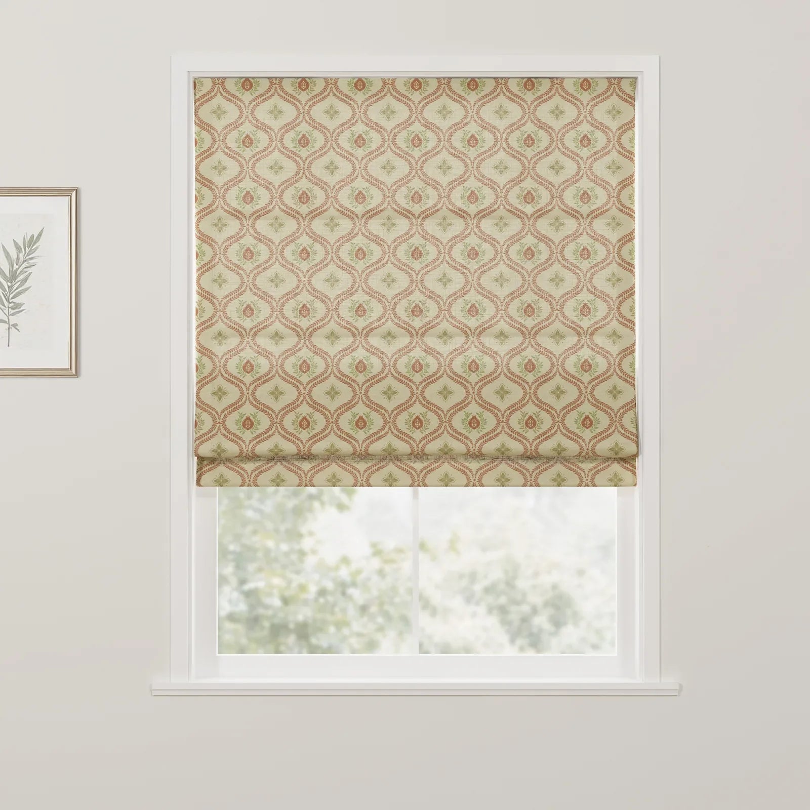 A Roman blind at a window featuring a beige background with a repeating pattern of terracotta red ovals and green leaf motifs, with a framed botanical print on the adjacent wall