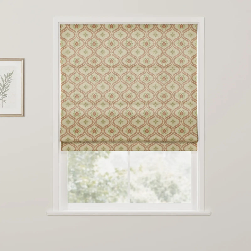 A Roman blind at a window featuring a beige background with a repeating pattern of terracotta red ovals and green leaf motifs, with a framed botanical print on the adjacent wall