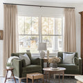 Tapioca Liz Linen Pleated Curtains framing a green sofa beneath a wide sunlit window