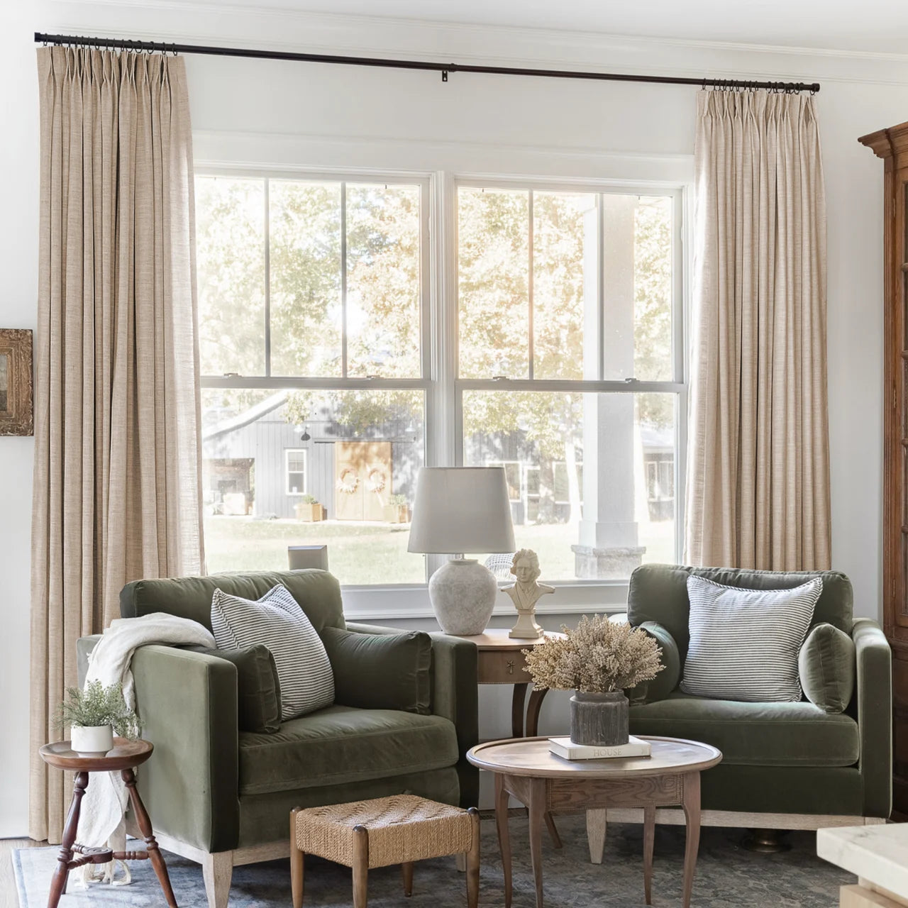 Tapioca Liz Linen Pleated Curtains framing a green sofa beneath a wide sunlit window