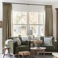 Taupe Grey Liz Linen Pleated Curtains framing a green sofa beneath a wide sunlit window