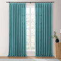 Teal textured floor-length curtains with pinch pleats on a black rod frame a bright window in an interior room, featuring a fluted wooden side table with a black vase and greenery