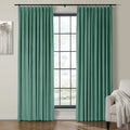 Photograph of a stylish room interior featuring two pleated seafoam green curtains on a black rod framing a large grid window, complemented by a minimalist grey tree artwork and a beige armchair with a white fringed throw