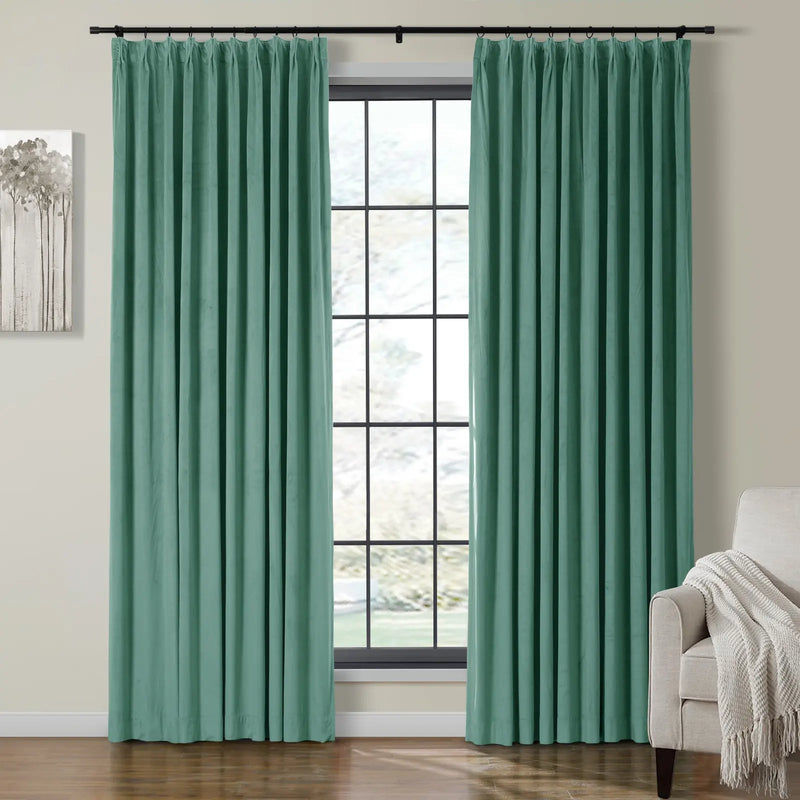 Photograph of a stylish room interior featuring two pleated seafoam green curtains on a black rod framing a large grid window, complemented by a minimalist grey tree artwork and a beige armchair with a white fringed throw
