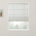 A white window features a grey and white striped roman blind partially raised, revealing blurred green trees outside and a framed landscape artwork on the adjacent wall