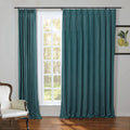 Teal linen pleated curtains on a black rod frame a multi-pane window with a bright green outdoor view beside a classic white tufted armchair and a framed lemon botanical print