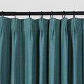 Photograph of a deep teal blue-green textured pleated curtain hung on a black rod with matching black rings
