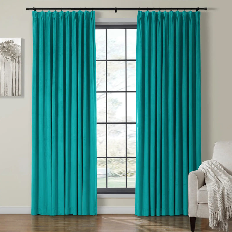 A pair of vibrant teal velvet curtains with grommet tops frames a large grid-pattern window in a modern room, flanked by an abstract gray tree artwork and a light beige armchair with a textured white throw