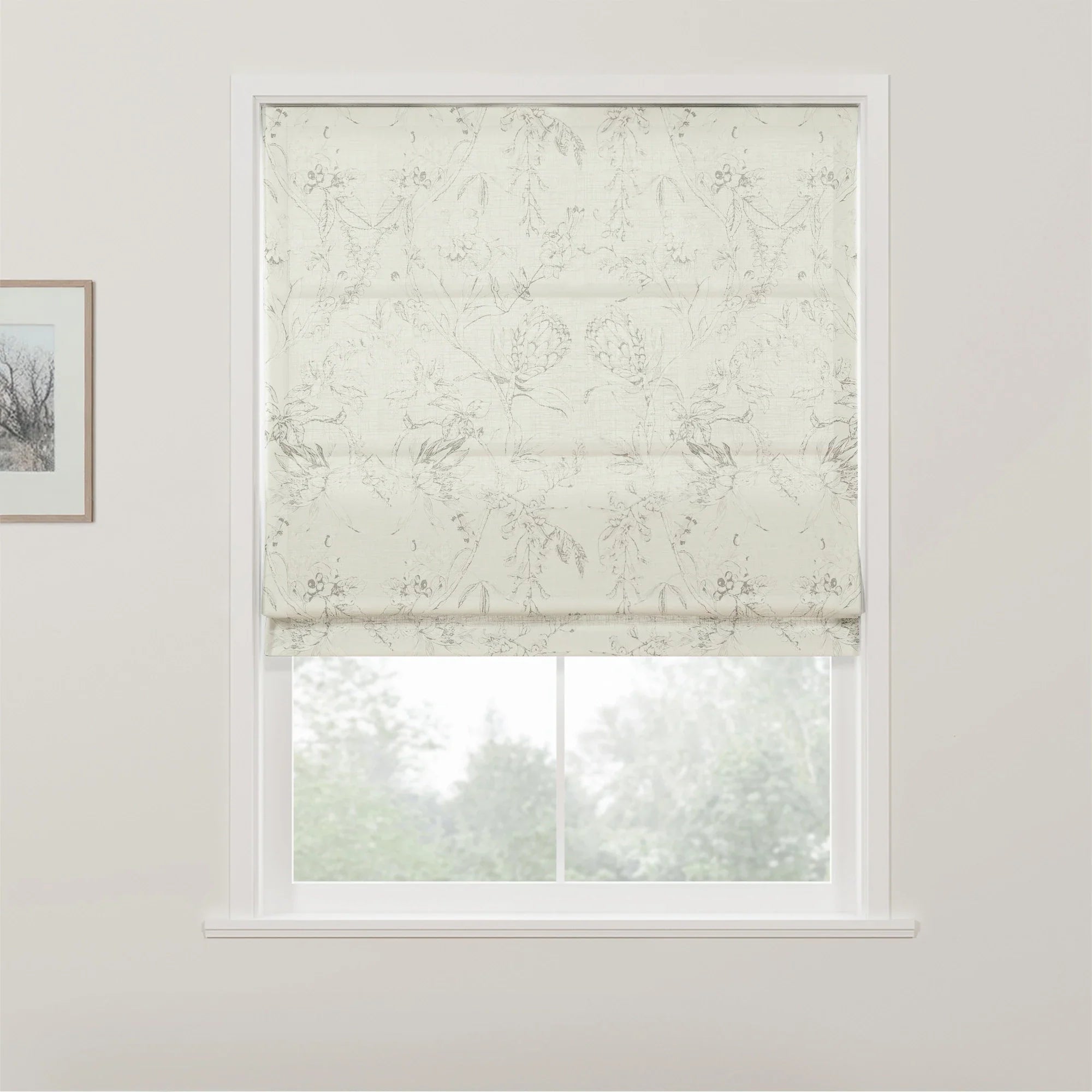 White Roman blind with subtle gray floral damask pattern covering a white-framed window, revealing blurred green trees outside from an interior setting