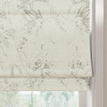 Fabric Roman blind with a delicate grey botanical sketch pattern of branches leaves and berries on off-white textured fabric lowered over a window with a blurred green garden view