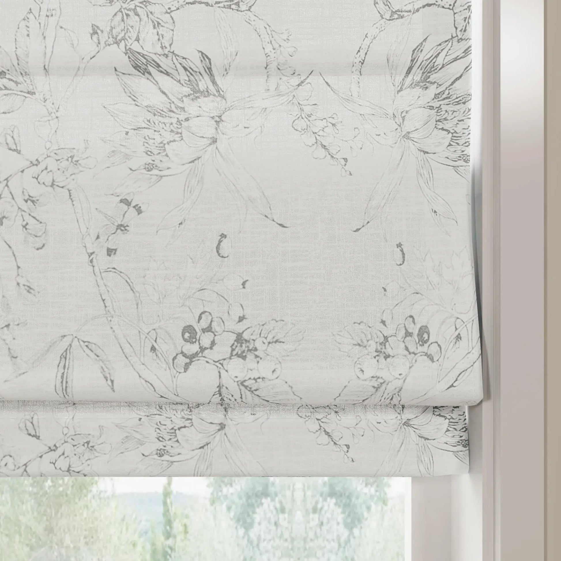 A partially lowered white textured fabric roman blind featuring a monochrome grey botanical sketch pattern of flowers and berries overlooking blurred outdoor greenery