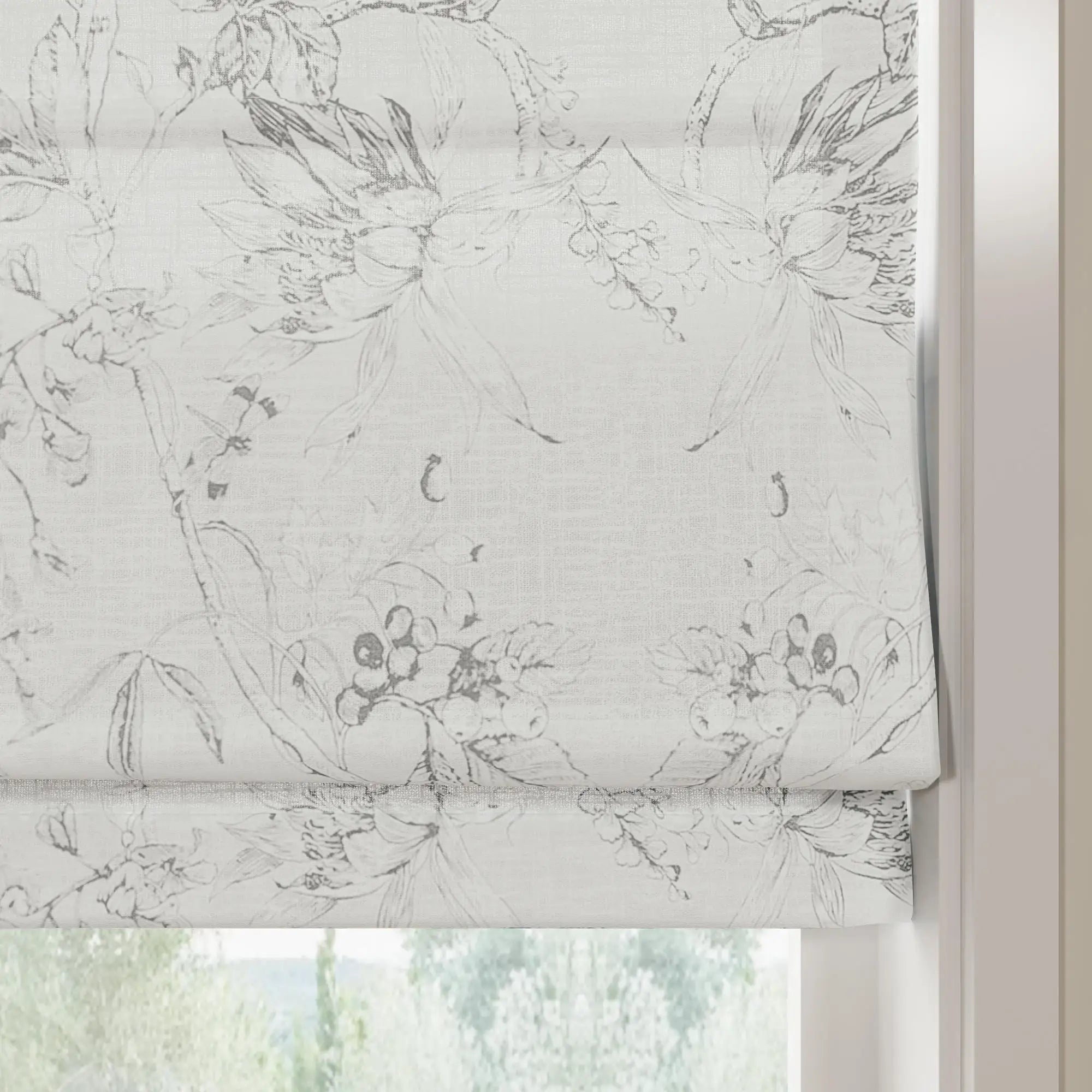 A partially lowered white textured fabric roman blind featuring a monochrome grey botanical sketch pattern of flowers and berries overlooking blurred outdoor greenery