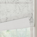 Fabric Roman blind featuring a delicate grey botanical outline pattern partially rolled up over a window revealing blurred green foliage outside