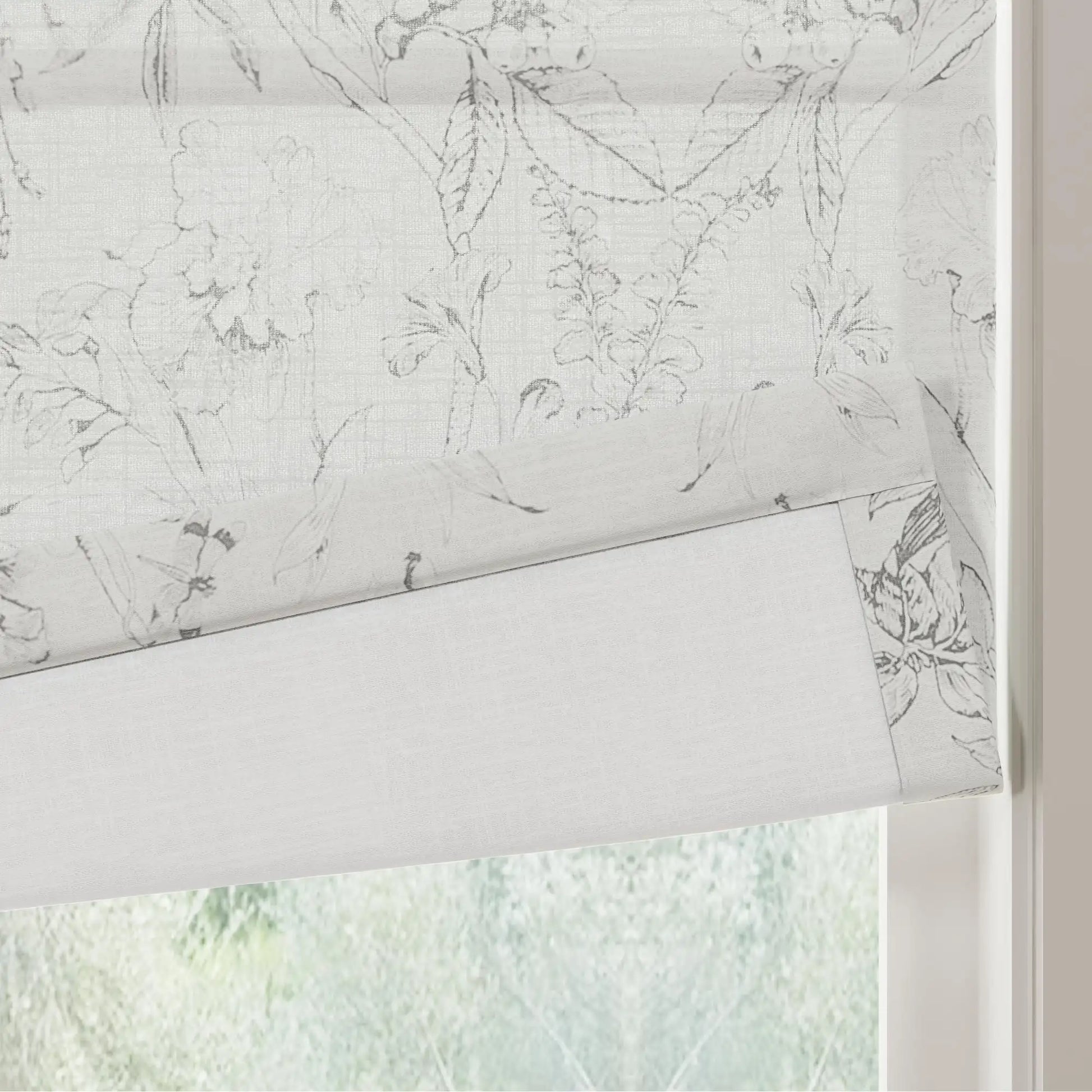 Fabric Roman blind featuring a delicate grey botanical outline pattern partially rolled up over a window revealing blurred green foliage outside