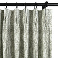 Photograph of a pleated white curtain with a repeating muted green leaf pattern, hung with black rings on a dark curtain rod
