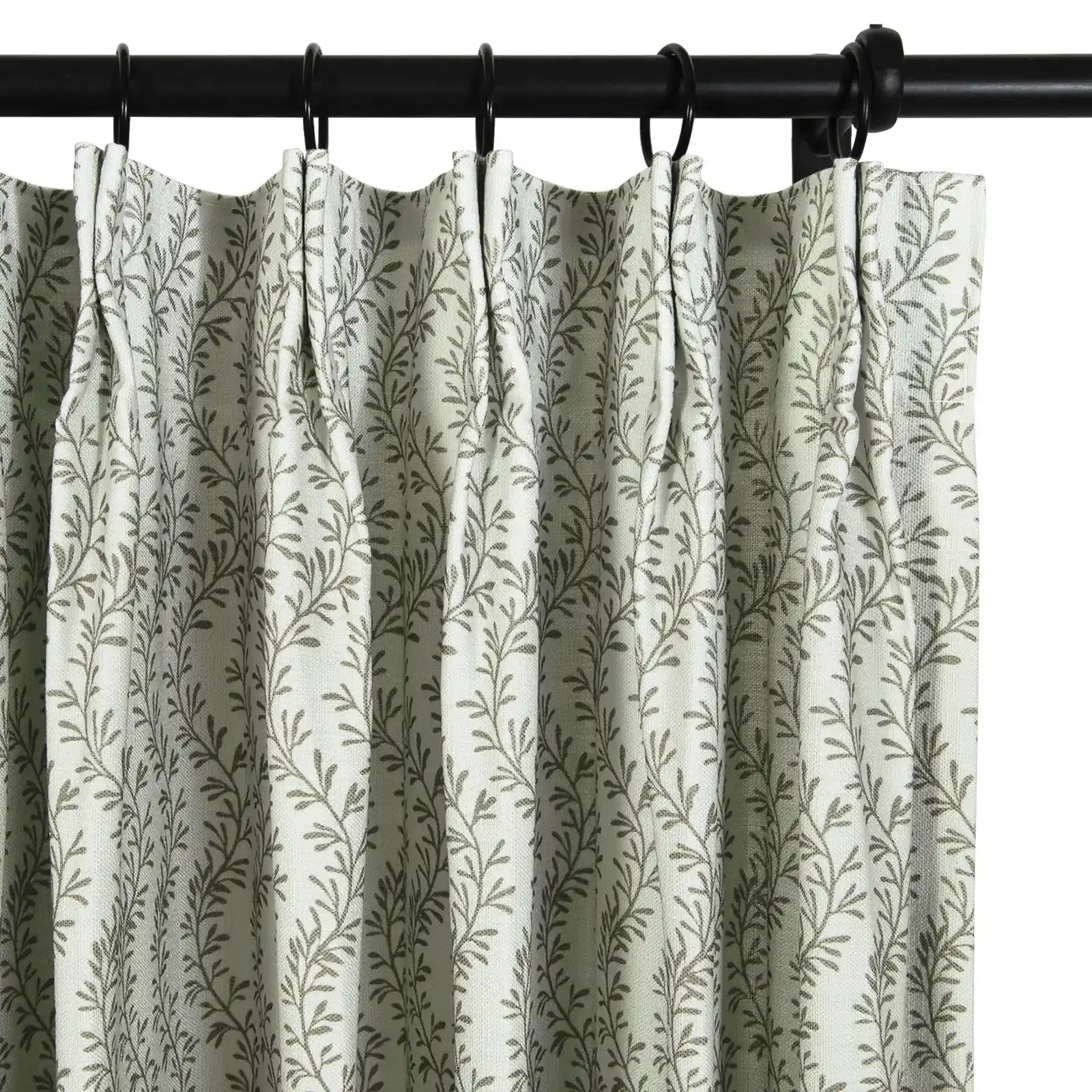 Photograph of a pleated white curtain with a repeating muted green leaf pattern, hung with black rings on a dark curtain rod