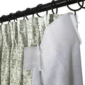 Close-up photograph of a black metal curtain rod with rings holding a pleated light green curtain featuring an olive leaf pattern alongside a white curtain liner secured by plastic hooks