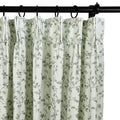 Light green pleated curtains featuring a delicate gray floral vine pattern suspended from a black curtain rod and rings