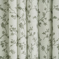 White fabric draped in vertical folds featuring a delicate green-grey floral pattern of intertwining vines and small blossoms