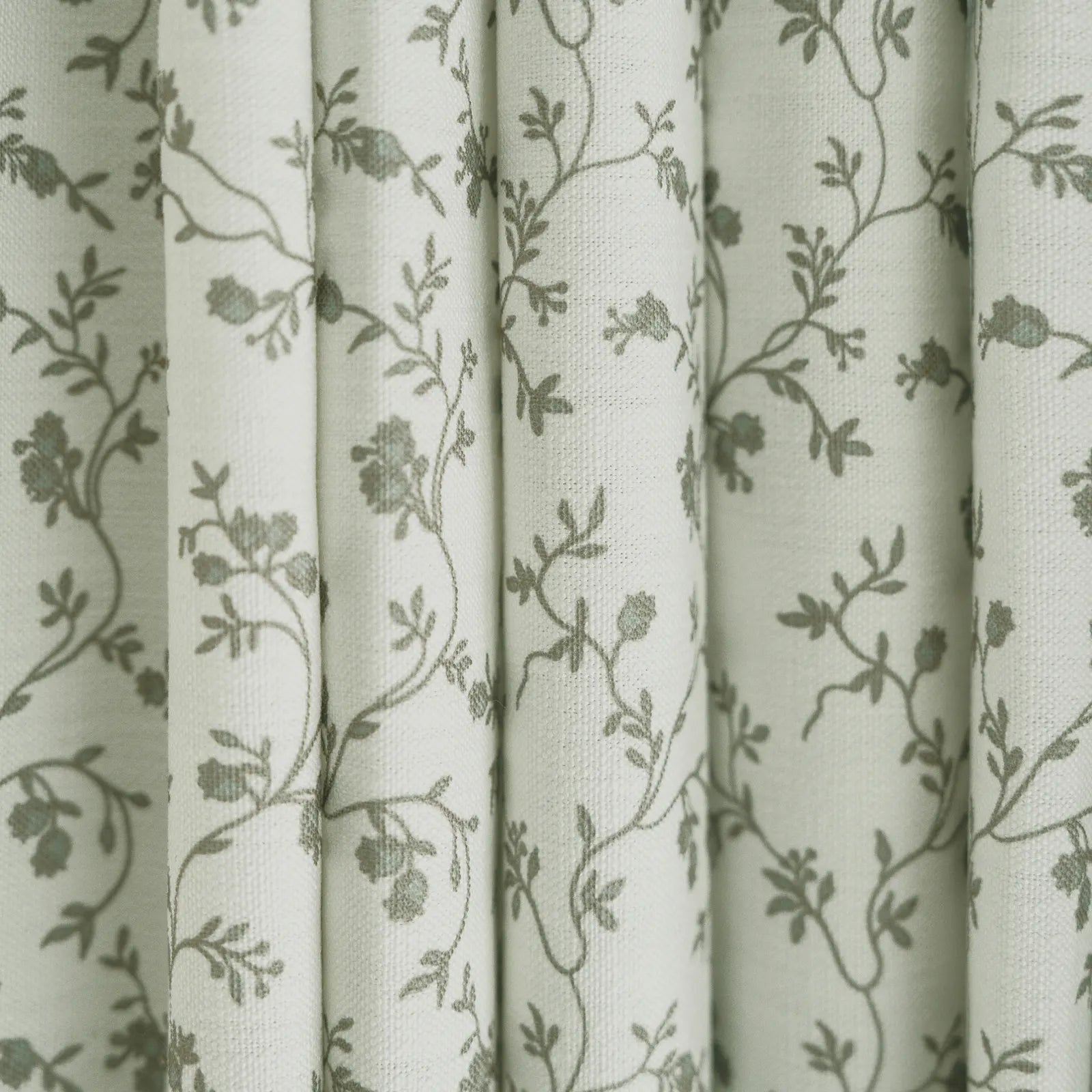 White fabric draped in vertical folds featuring a delicate green-grey floral pattern of intertwining vines and small blossoms
