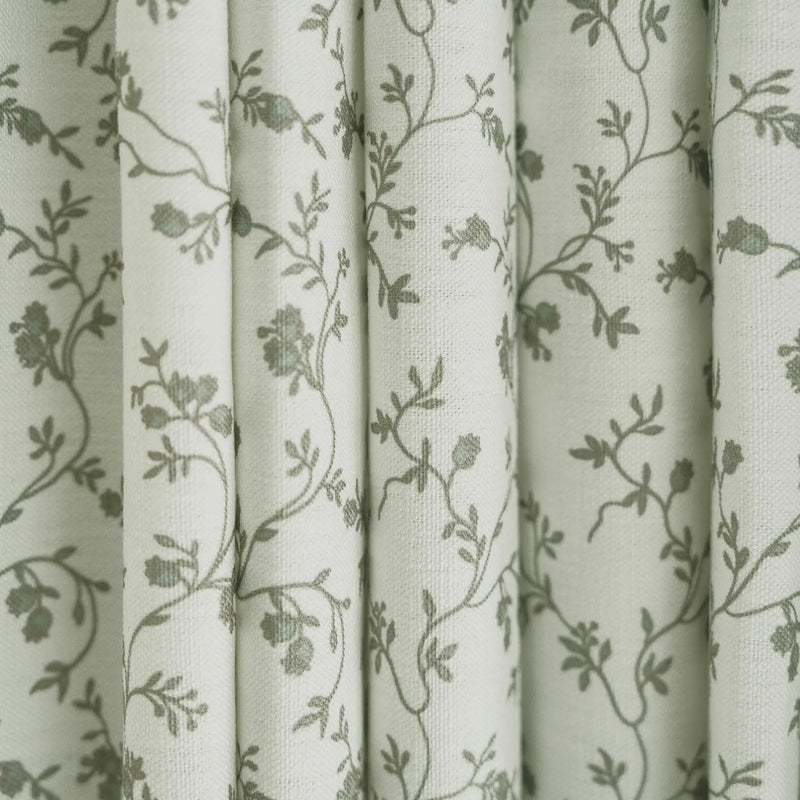 White fabric draped in vertical folds featuring a delicate green-grey floral pattern of intertwining vines and small blossoms