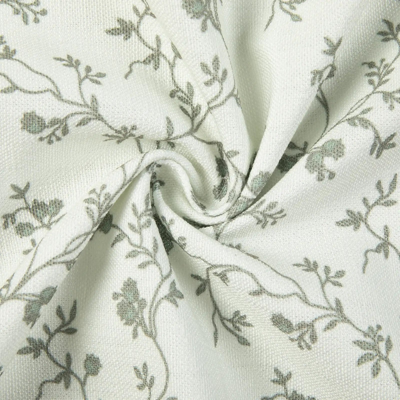 Textured white fabric featuring a delicate, repeating gray-green vine and floral pattern with soft swirling folds