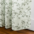 Fabric light green textured textile featuring a delicate grey-green floral vine pattern draped near a warm wooden floor and white baseboard