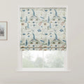 Textile Roman blind featuring a delicate floral pattern with blue lupine-like spikes, creamy white blossoms with orange centers, and small red flowers, set in a bright window against a backdrop of blurred green trees