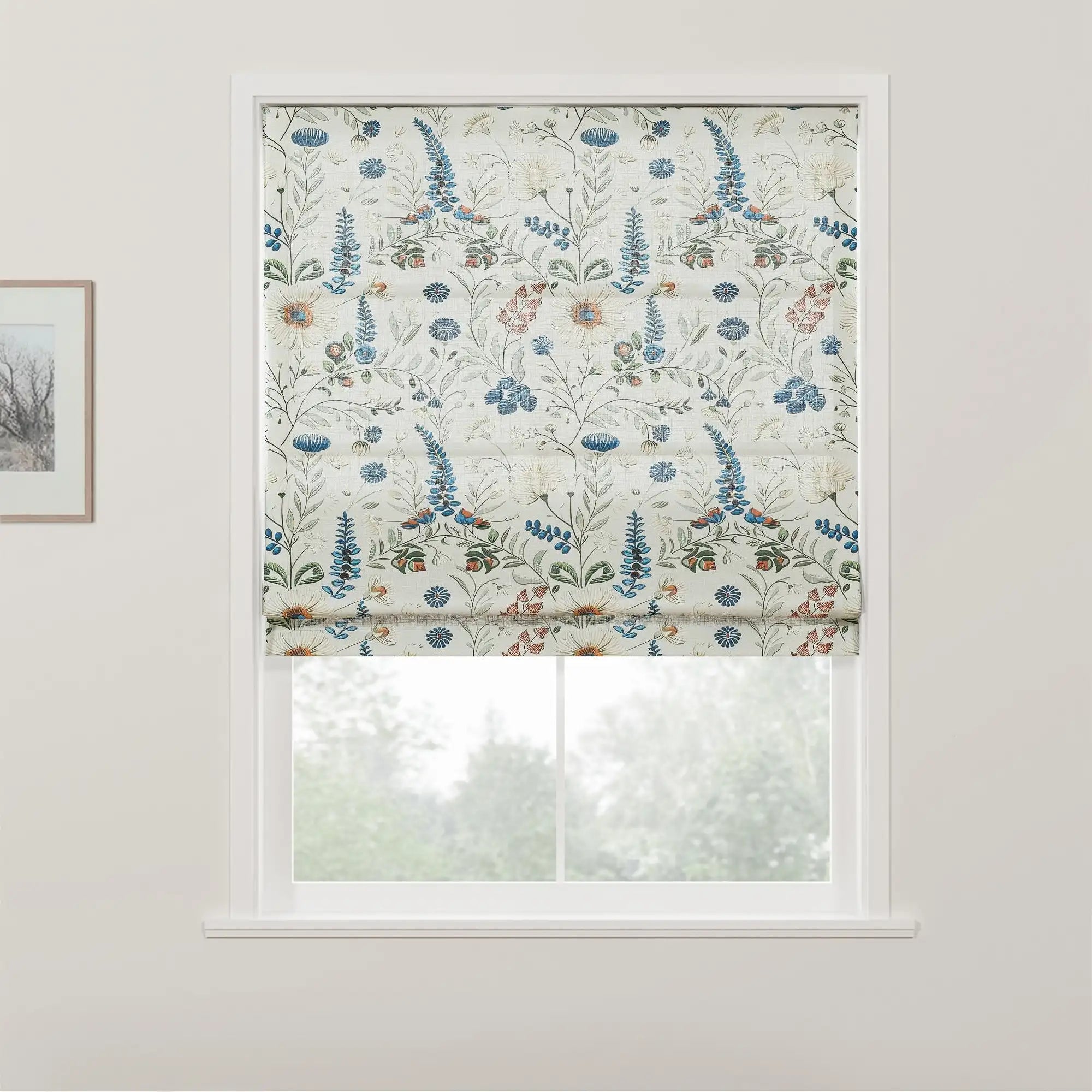 Textile Roman blind featuring a delicate floral pattern with blue lupine-like spikes, creamy white blossoms with orange centers, and small red flowers, set in a bright window against a backdrop of blurred green trees