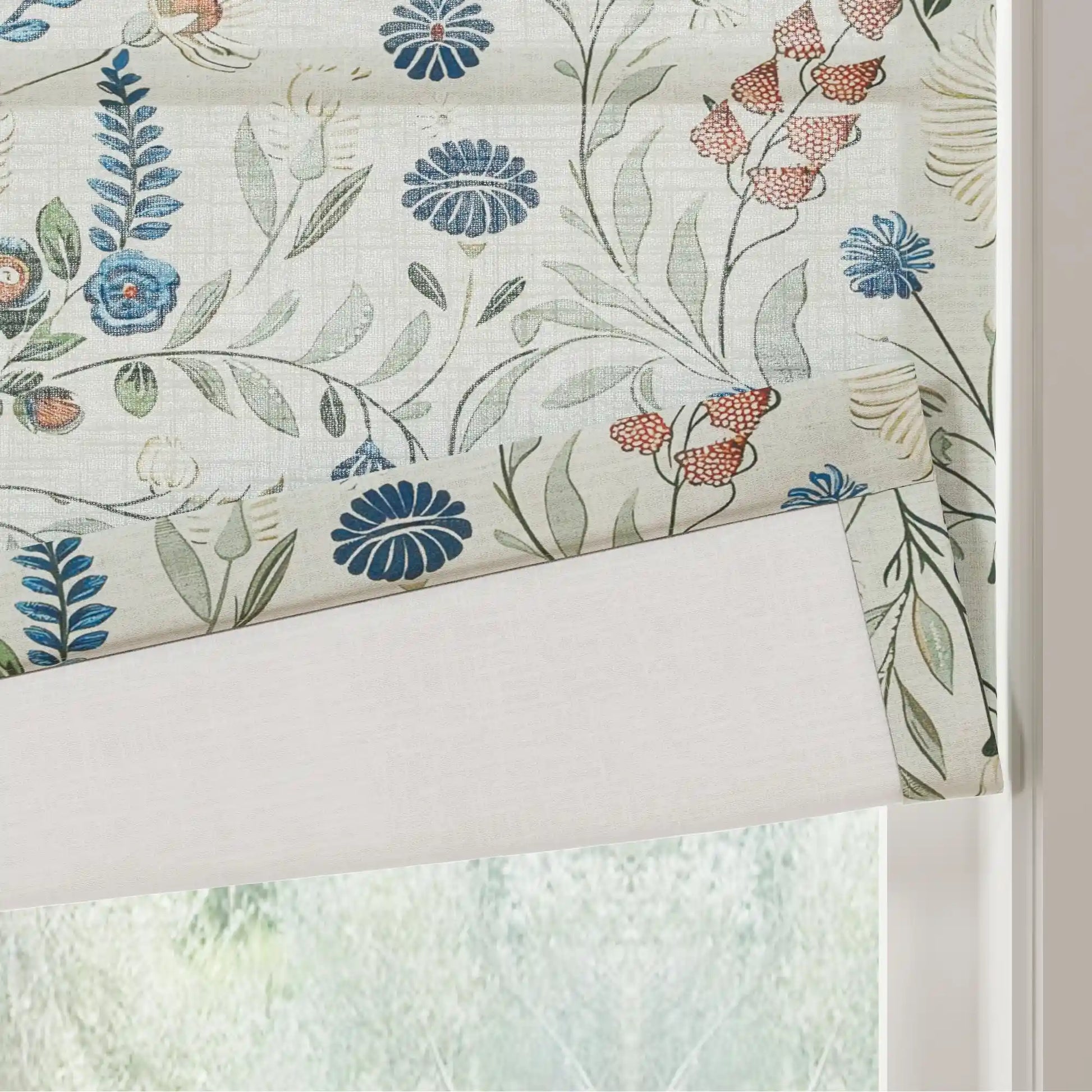 A partially unfurled Roman blind in a window featuring a botanical floral pattern with dark blue stylized chrysanthemums bright blue fern-like leaves and clusters of coral berries on a light textured fabric revealing a plain white lining
