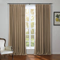 Beige pleated drapes on a black rod frame a white multi-paned window revealing bright green trees outside with a classic white upholstered chair and a framed lemon botanical print completing the room
