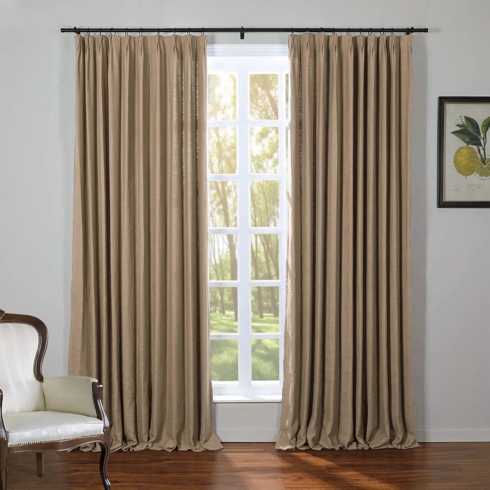 Beige pleated drapes on a black rod frame a white multi-paned window revealing bright green trees outside with a classic white upholstered chair and a framed lemon botanical print completing the room