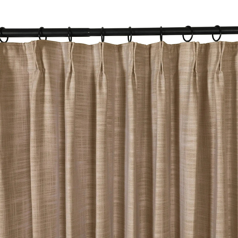 Photograph of a tan textured linen-look pleated curtain hanging from a black rod with rings