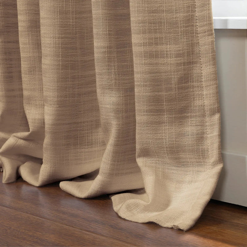 A close-up of natural beige woven linen-look curtains with visible texture softly puddling on a rich dark wooden floor next to a crisp white wall trim