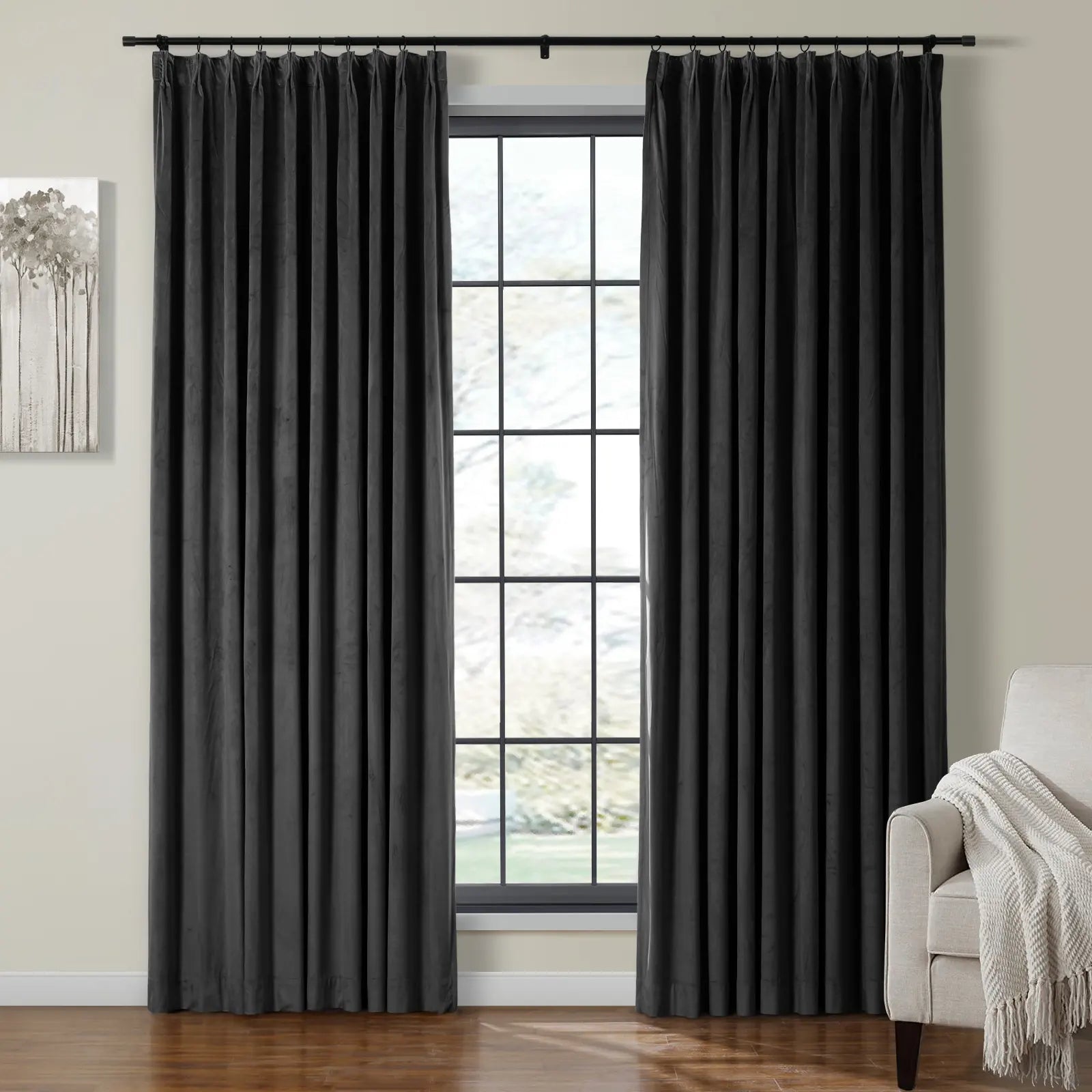 Black velvet pleated curtains hang on a dark rod framing a window in a modern room decorated with abstract gray tree artwork and a beige armchair