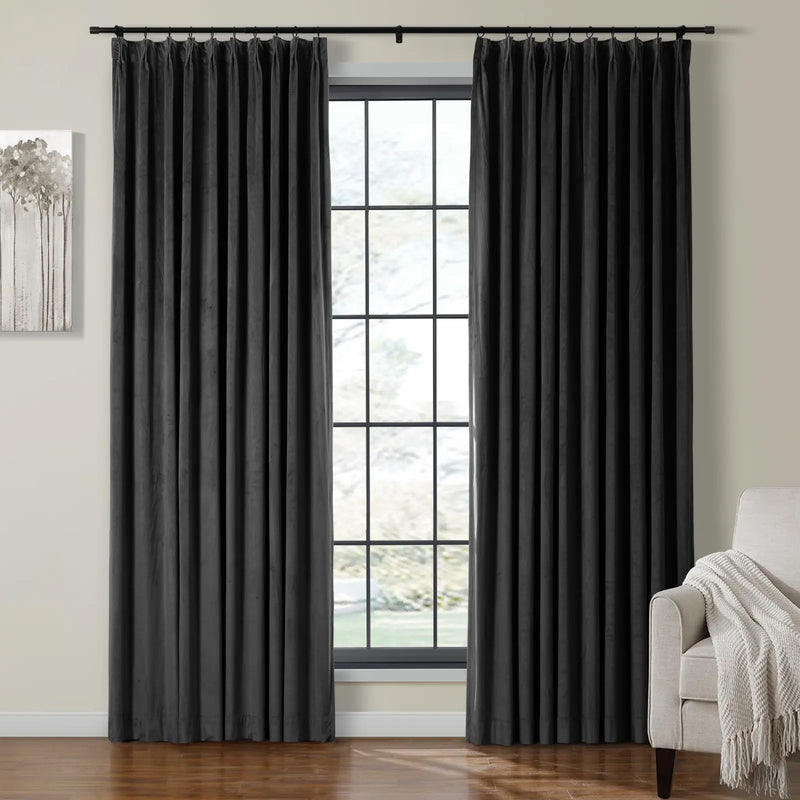 Black velvet pleated curtains hang on a dark rod framing a window in a modern room decorated with abstract gray tree artwork and a beige armchair