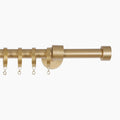 Photograph of a modern metallic gold curtain pole with several infinity loop hanging rings a central wall mount and a simple cylindrical finial