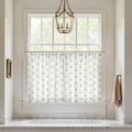 Bathroom window above a white built-in tub featuring a white valance curtain with a golden paisley pattern, a brass lantern chandelier, and a white marble surround
