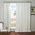 Bright room with white textured drapes on a black rod framing a grid-paned window looking out to a green field, featuring a classic wooden armchair with white upholstery and brass nailhead trim, and a framed lemon botanical print on the gray wall