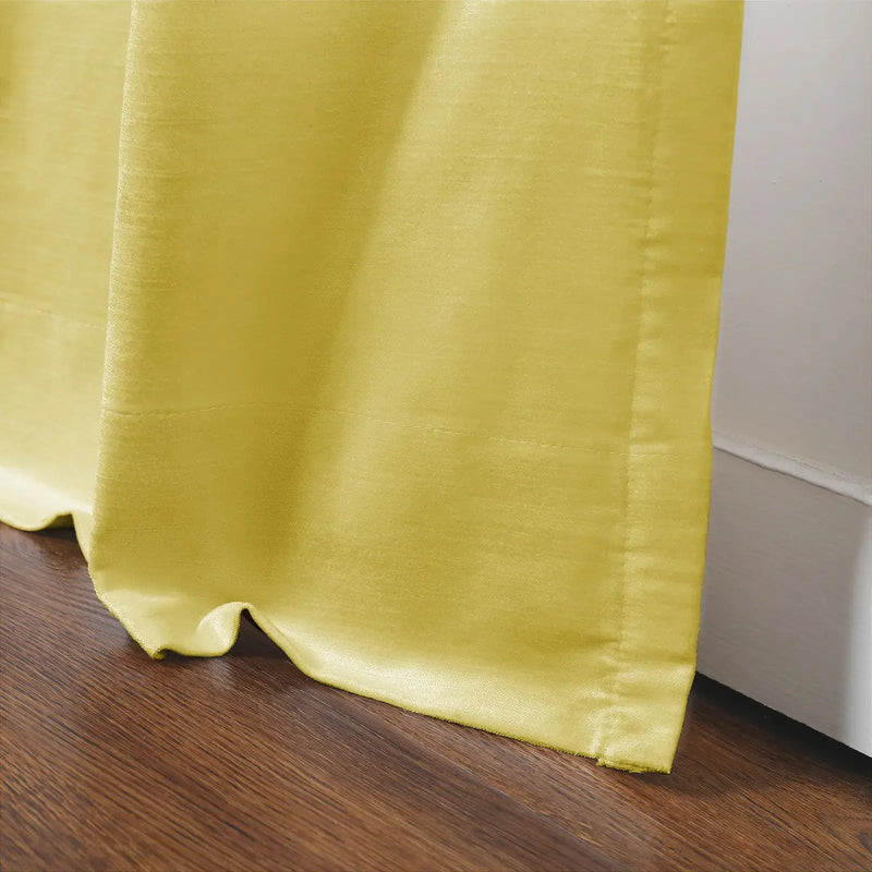 Vibrant chartreuse yellow curtain fabric with a subtle sheen puddled elegantly on a rich brown wood floor next to a crisp white baseboard