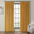 Mustard yellow velvet pleated curtains frame a large multi-pane window with black grid in a modern living room featuring abstract grey tree artwork and a beige armchair with a white textured throw