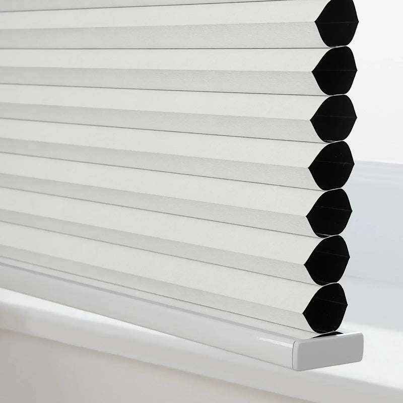 White cellular Blinds with textured pleated fabric and visible black honeycomb cells on a sleek silver bottom rail resting on a white window sill