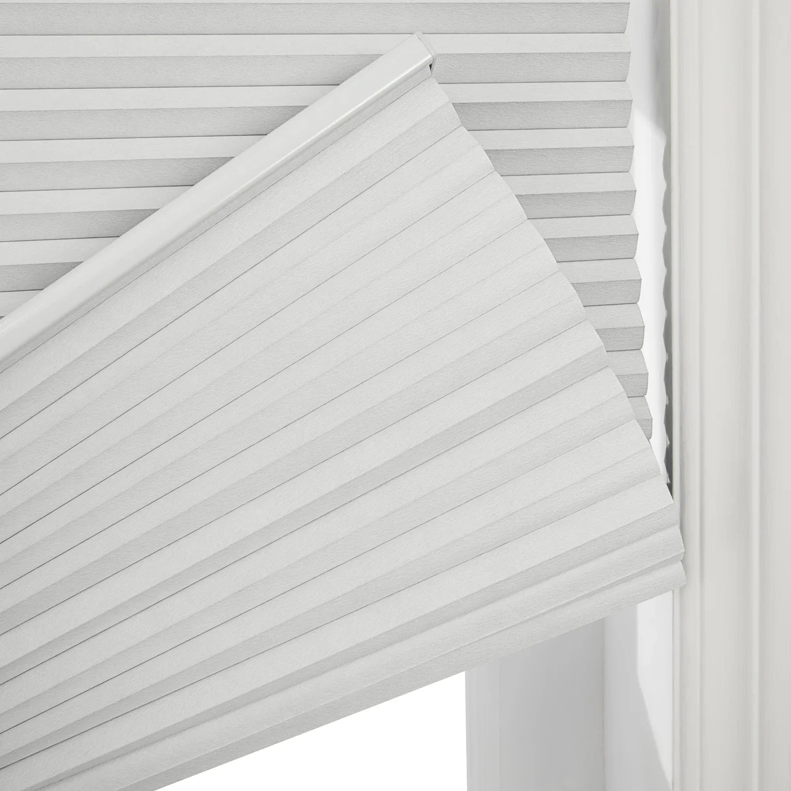 Light grey textured cellular window Blinds partially lowered to reveal their crisp pleated structure within a bright white window frame