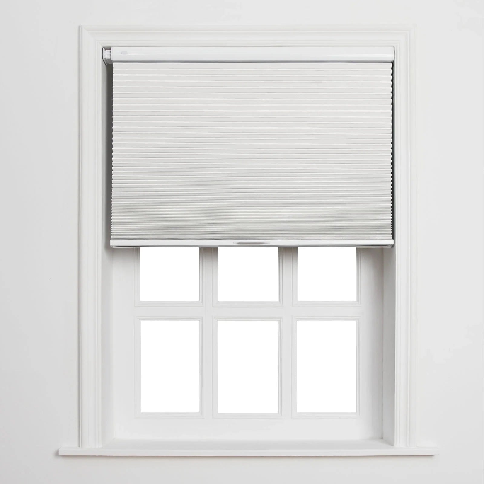 A modern interior features a partially lowered white cellular window Blind above a six-pane white window frame and sill against a minimalist white wall