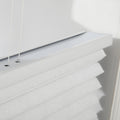 Close-up of white textured honeycomb cellular Blinds featuring a visible headrail with thin white adjustment cords and soft pleated fabric illuminated by natural light