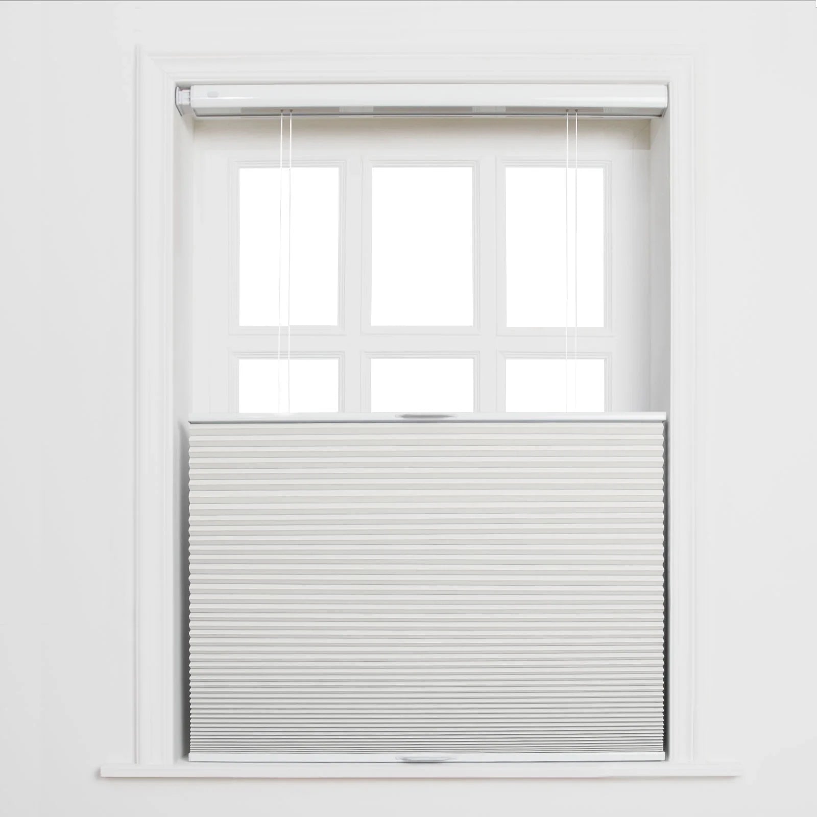 A white paneled window in an interior room featuring light grey top-down bottom-up cellular Blinds with sheer white pull strings and bright light through the upper panes